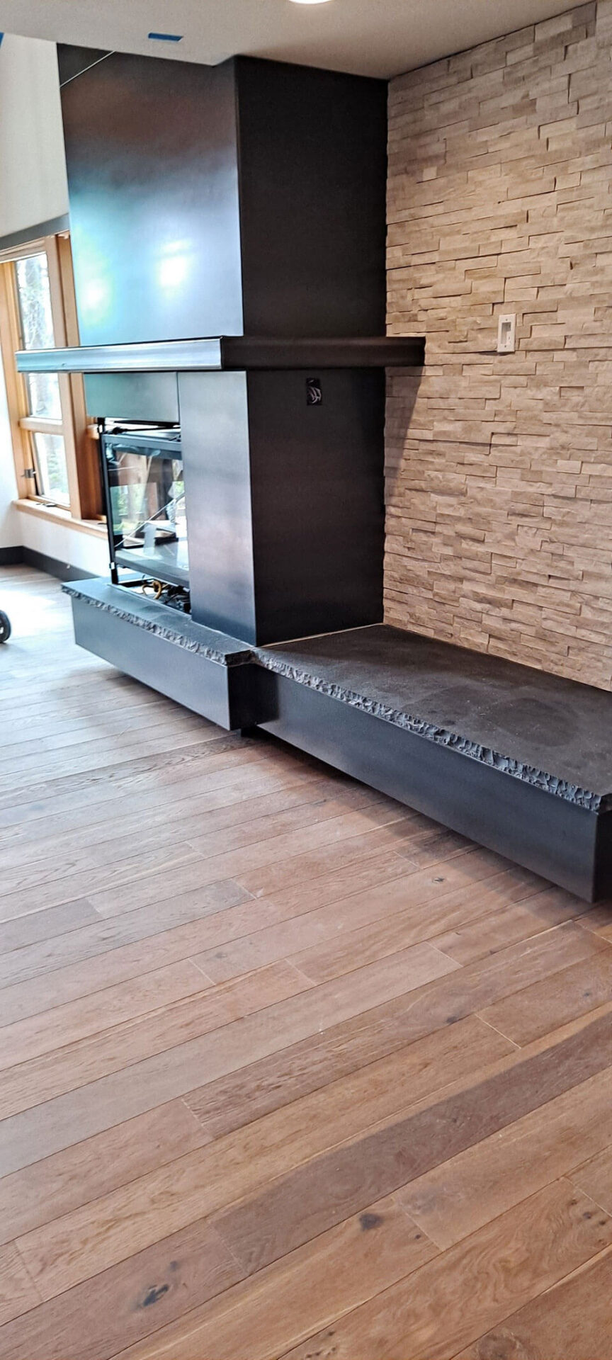 A modern living room corner with a black metal and stone fireplace, stone accent wall, and light wood flooring.
