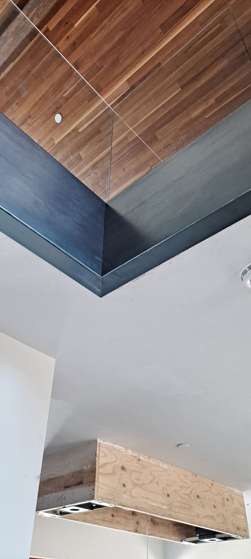 Ceiling view featuring a mix of wood paneling, white drywall, and a partially finished plywood structure, with a smoke detector visible.