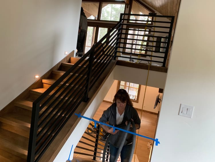 A person uses blue painter's tape on a staircase railing in a multi-story home under construction or renovation.