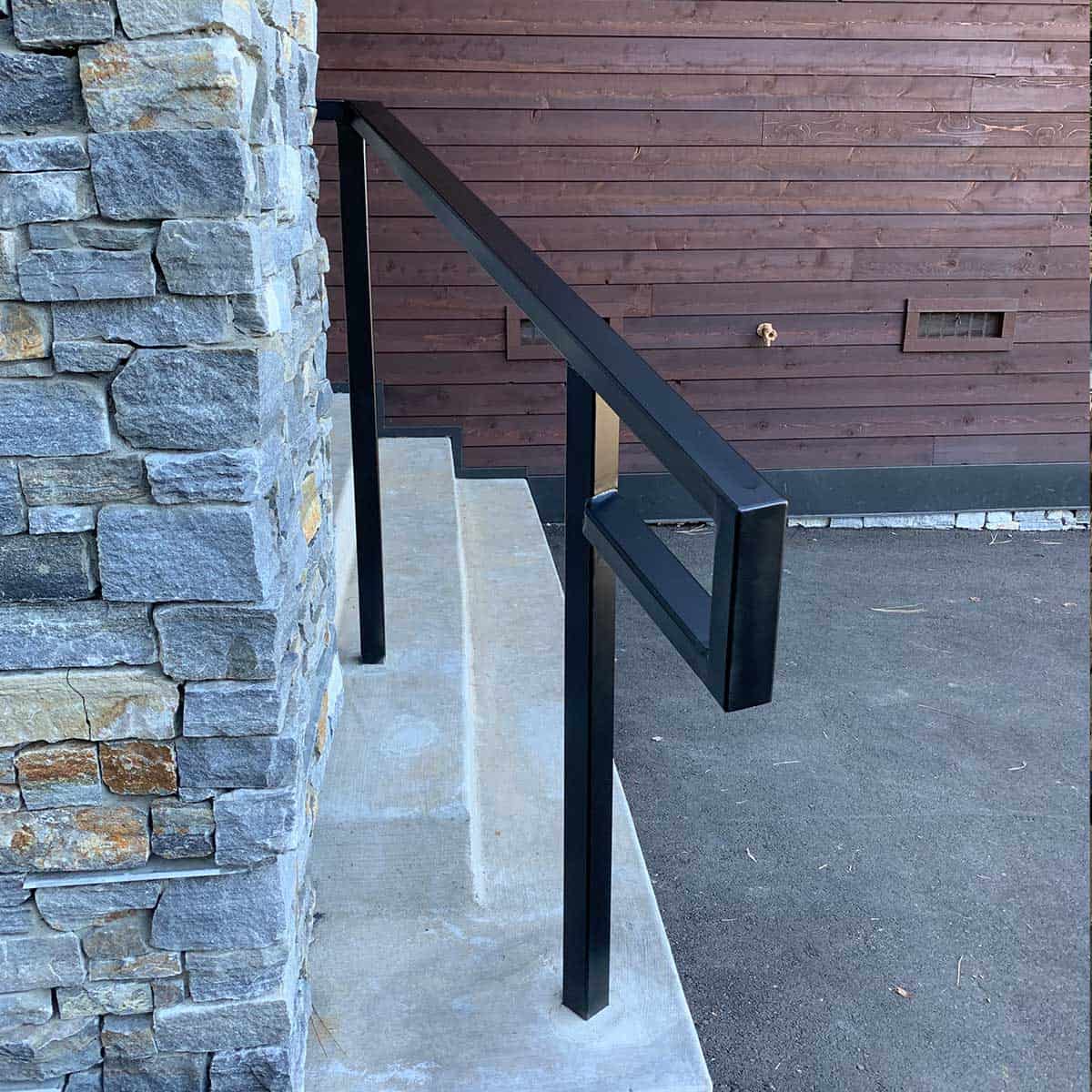 Concrete steps with a metal handrail beside a stone wall and a wooden exterior wall.